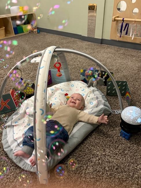 An infant on a play mat watching bubbles float overhead