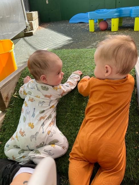 Two infants crawling on the turf outside