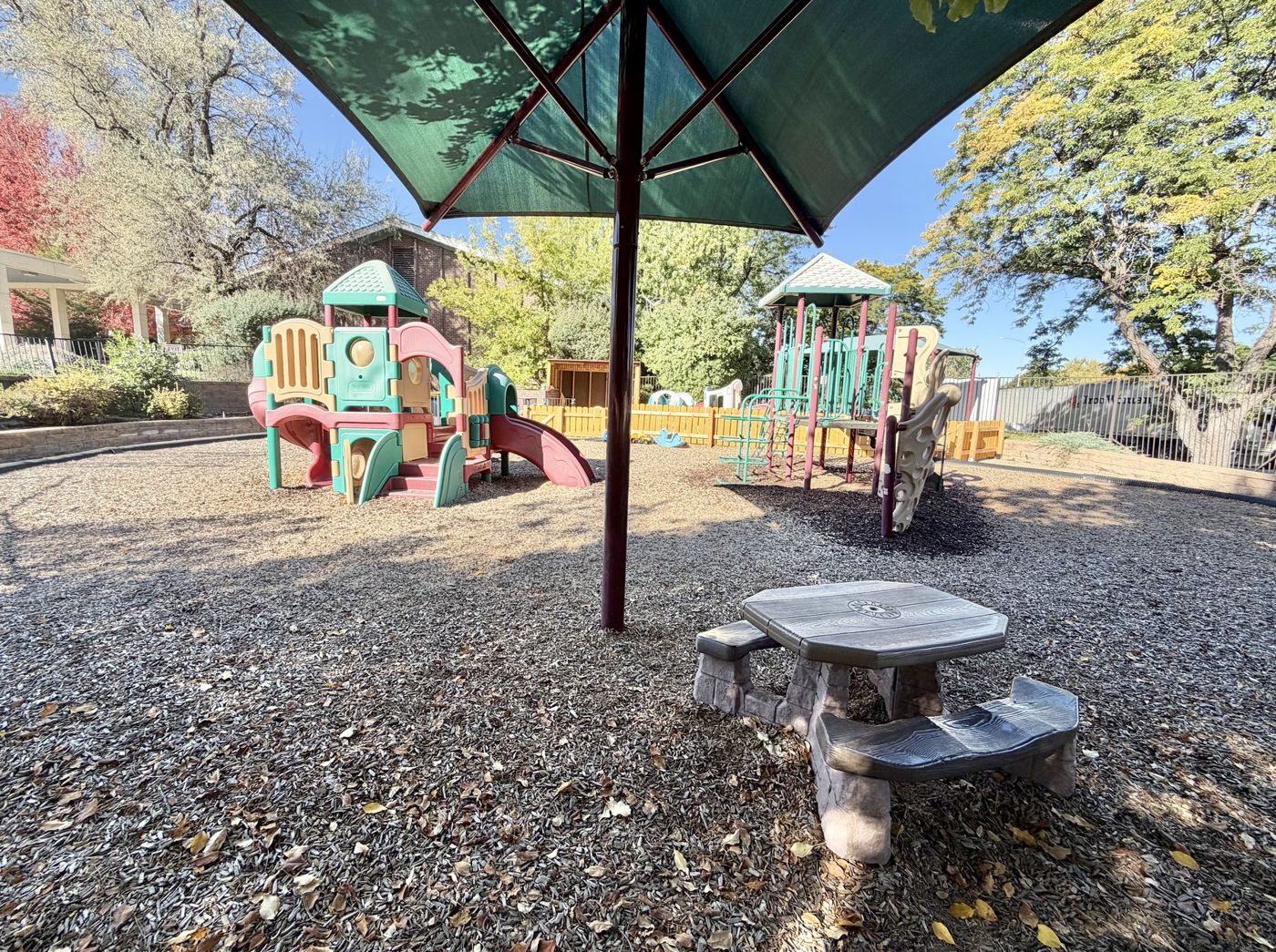 A shaded picnic table and play structures under big trees